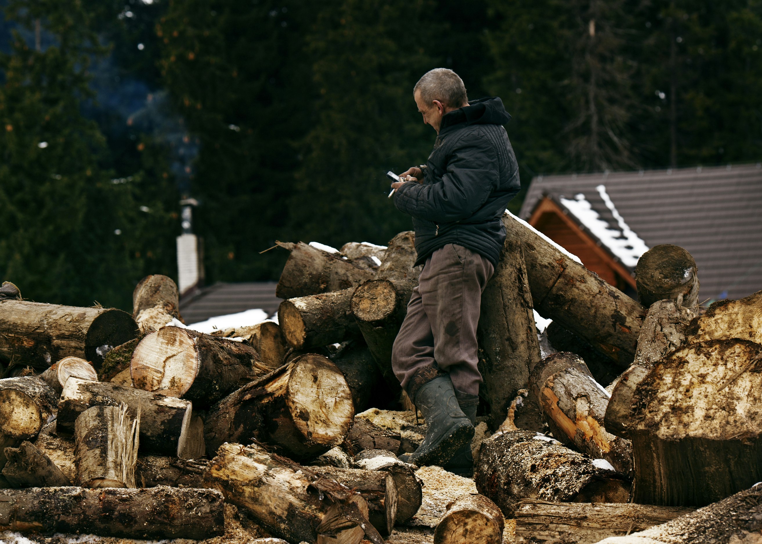 man in black jacket and brown pants sitting on brown log during daytime